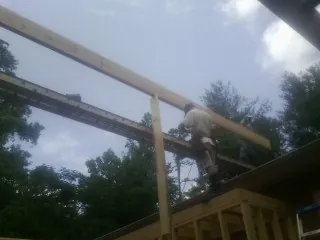 Carpenter setting a ridge beam over a new addition frame in Williamston