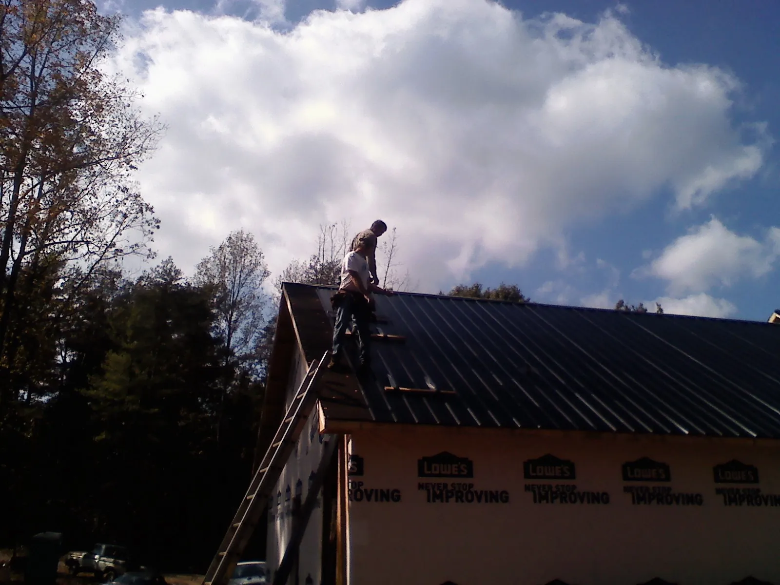 Roofer fastening dark metal panels high against a cloudy sky, from a Roof Inspection job in Williamston