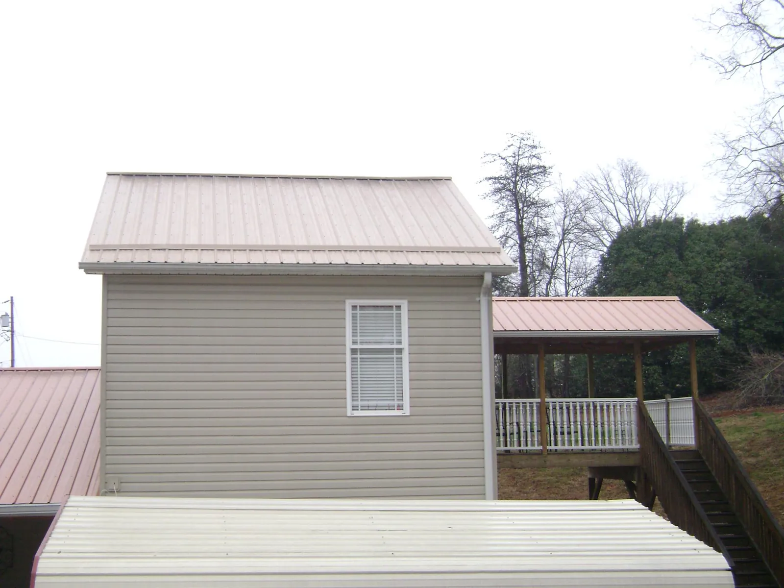 Tan metal roofs on a two story addition and attached porch, from a Roof Replacement job in Williamston